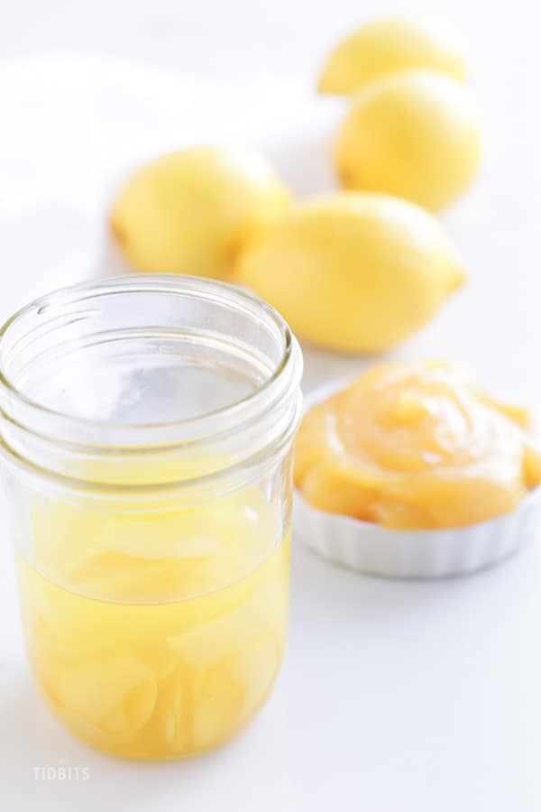 A jar of lemon extract with lemons in the background