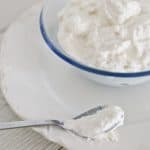 A spoon full of ricotta cheese next to a glass bowl