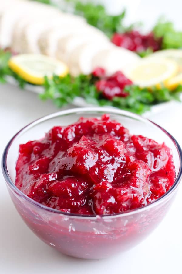 Glass bowl with cranberry sauce and a plate of turkey in the background