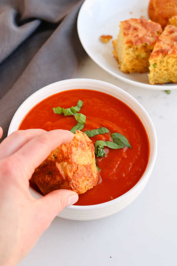 A piece of bread being dipped into a bowl of tomato soup