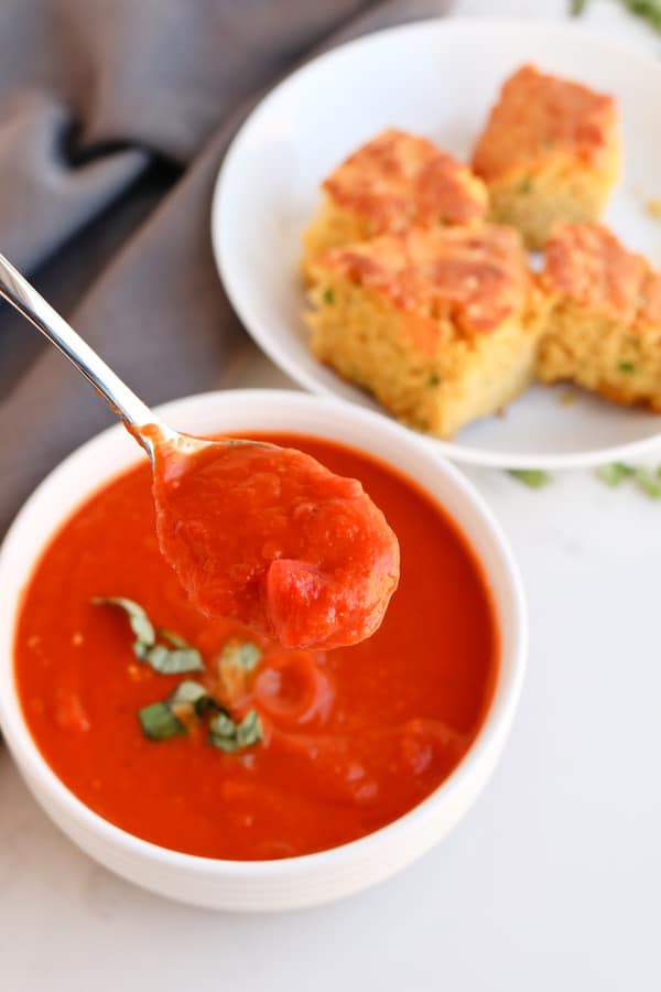 A spoonful of tomato soup being held towards camera