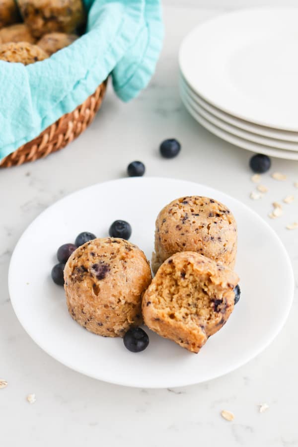 Three blueberry oatmeal muffins on a white plate, one with a bite taken out