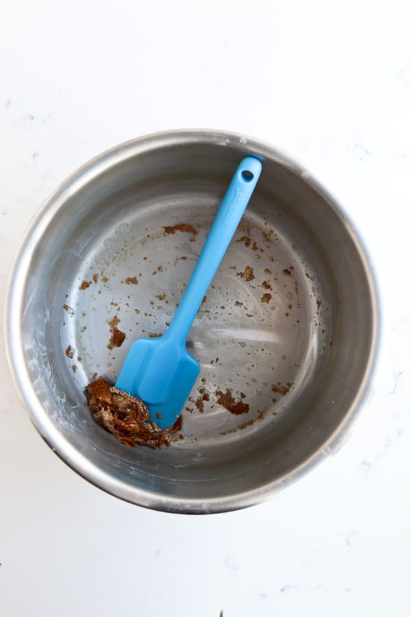 A blue spatula in an instant pot scraping off burnt mess