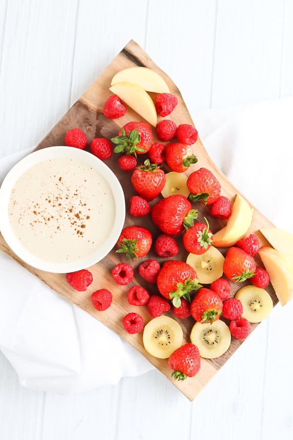 Strawberries and raspberries next to a white bowl of fruit dip