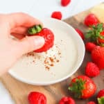 Strawberries and raspberries next to a white bowl of fruit dip