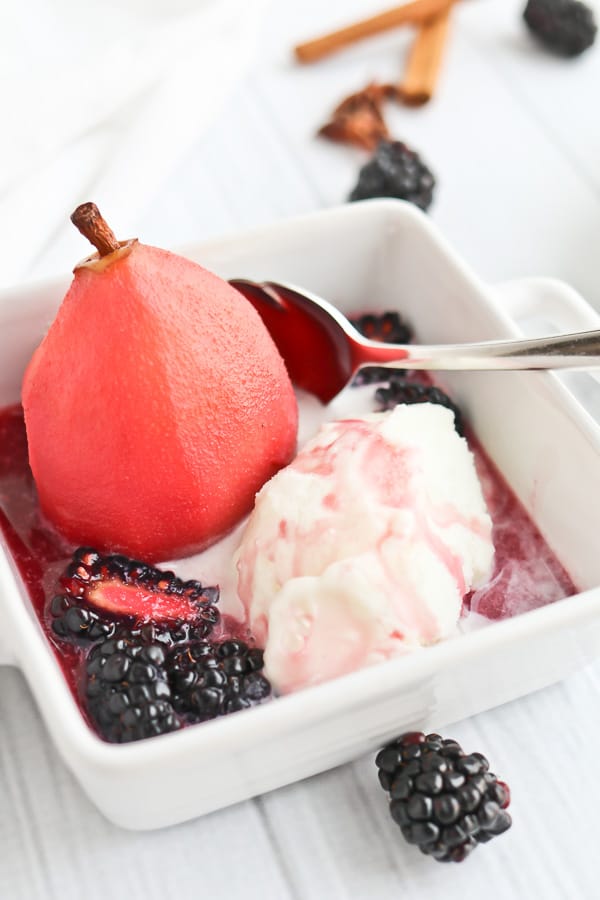 Poached pear in a white bowl with ice cream