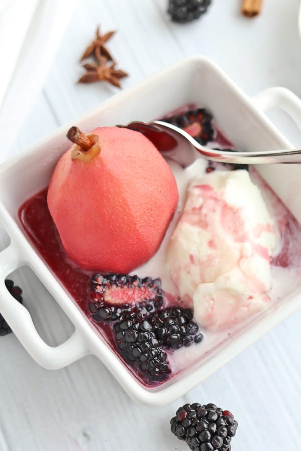 Poached pear in a white bowl with ice cream