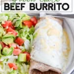 Burrito with white sauce and cheese next to a salad of lettuce, tomatoes, and avocado