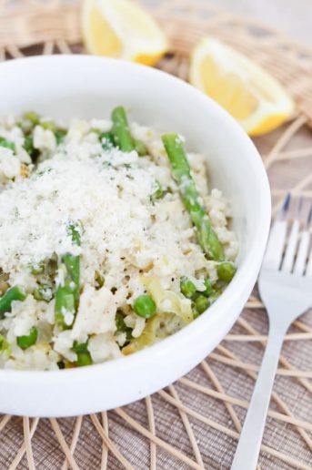 Instant Pot Lemon Risotto with Asparagus and Peas in a white bowl with a fork and lemon slices