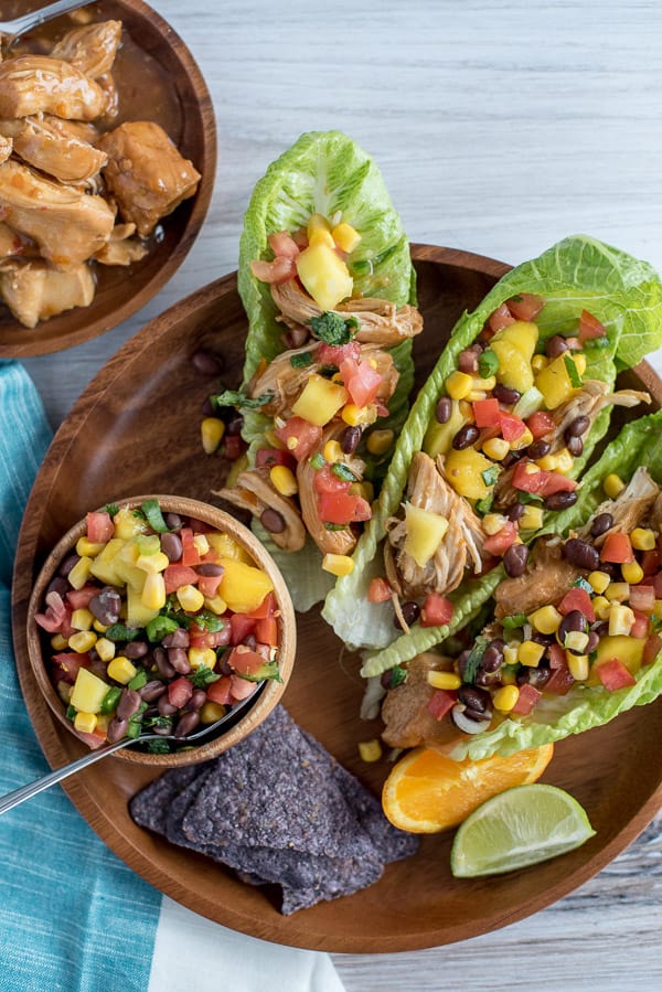 Instant Pot Orange Chicken with Mango Black Bean Salsa in lettuce wraps on a wood plate