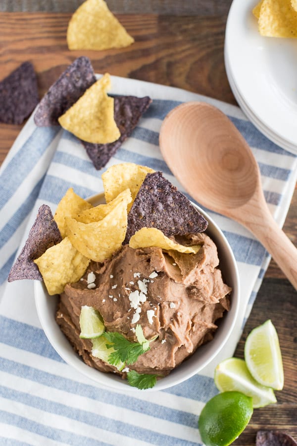 instant pot refried beans in a white bowl with chips and lime wedges