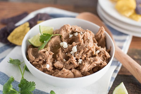 instant pot refried beans in a white bowl with chips and lime wedges