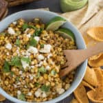 Large bowl of Mexican Street Corn Salad with cheese and lime wedges