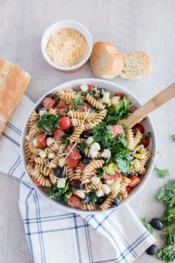 pasta salad with olives, pepperoni, cheese, kale, and cucumber in a white bowl