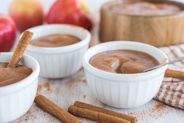 applesauce in white cups with apples and cinnamon sticks in the background