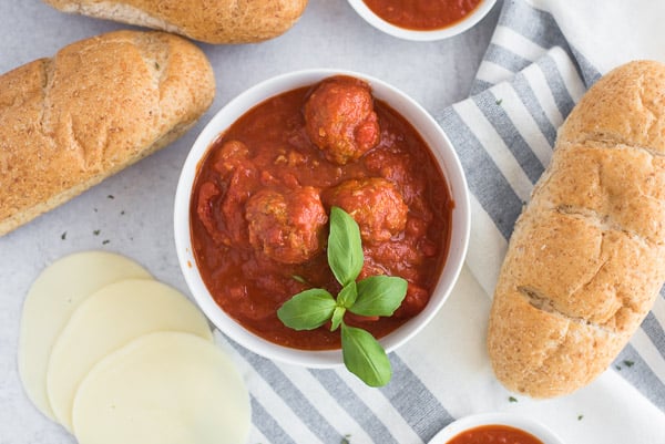 Meatballs in marinara sauce surrounded by rolls and cheese