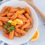 honey glazed carrots in a white bowl topped with an orange wedge and parsley