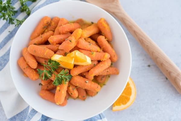 honey glazed carrots in a white bowl topped with an orange wedge and parsley