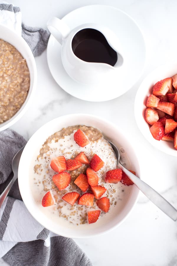 bowl of steel cut oatmeal with strawberries and cream and a bowl of strawberries
