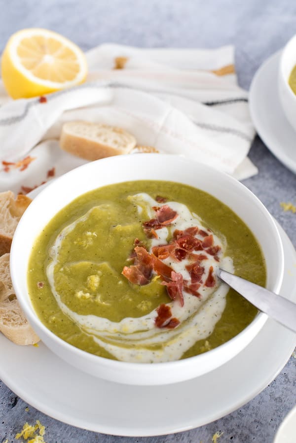Green asparagus soup with yogurt, bacon, and a lemon slice in a white bowl