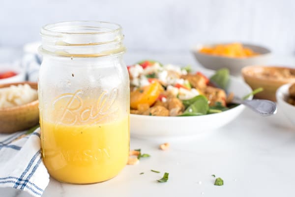 Orange vinaigrette in a mason jar in front of a salad