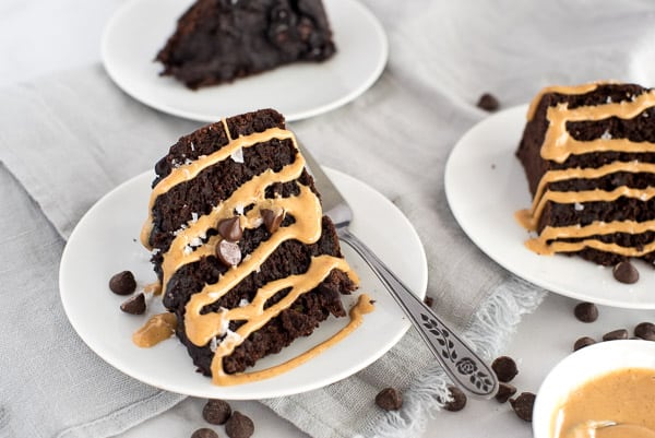 chocolate zucchini cake on a white plate drizzled with peanut butter