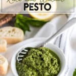 White bowl of pesto with a spoon and bread slices in the background