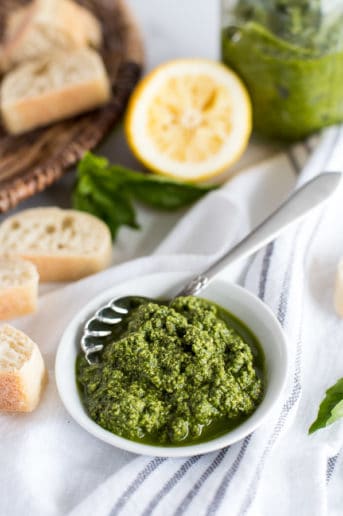 White bowl of pesto with a spoon and bread slices in the background