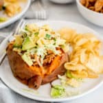 BBQ chicken stuffed sweet potato with avocados and cheese on a white plate