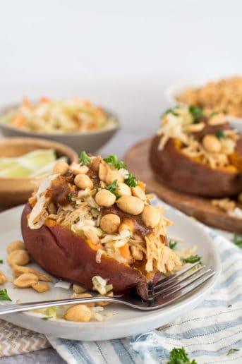 sweet potato on a white plate filled with coleslaw, peanuts, and peanut sauce