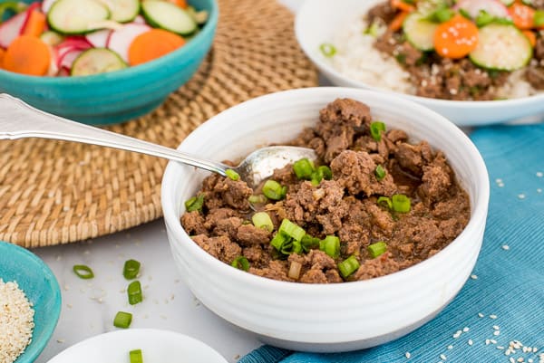 Korean Beef in a white bowl with a bowl of carrots, cucumbers, and radishes near by.