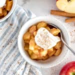 white bowl of cinnamon spiced apples topped with cream and cinnamon