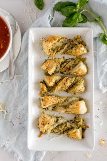 twisted pesto breadsticks on a white plate near a bowl of tomato soup