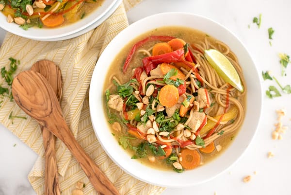 White bowl with thai soup with noodles, peppers, and cilantro