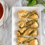 twisted pesto breadsticks on a white plate near a bowl of tomato soup