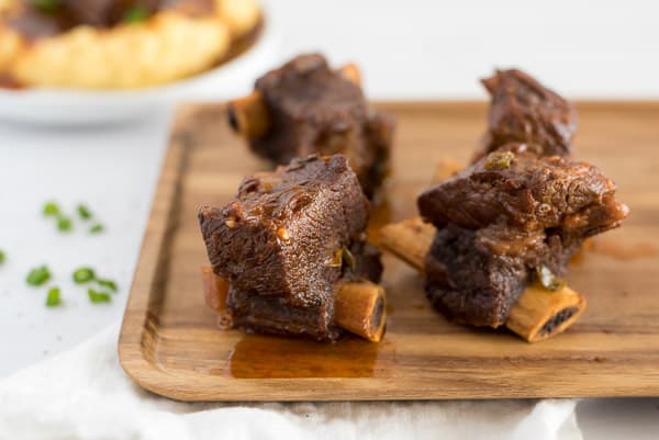 cutting board with 4 short ribs next to a plate of polenta