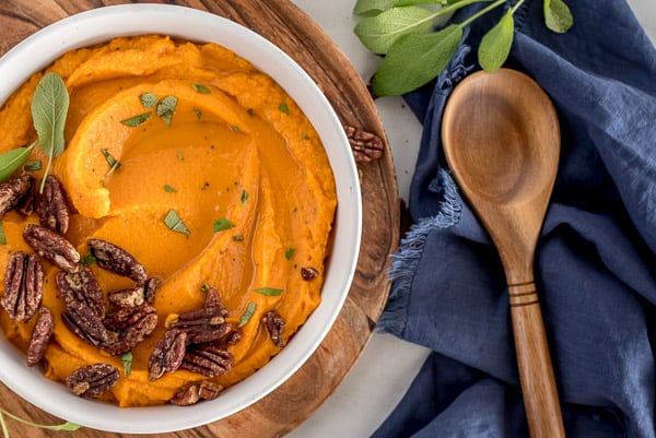 White bowl of mashed sweet potatoes with pecans on top