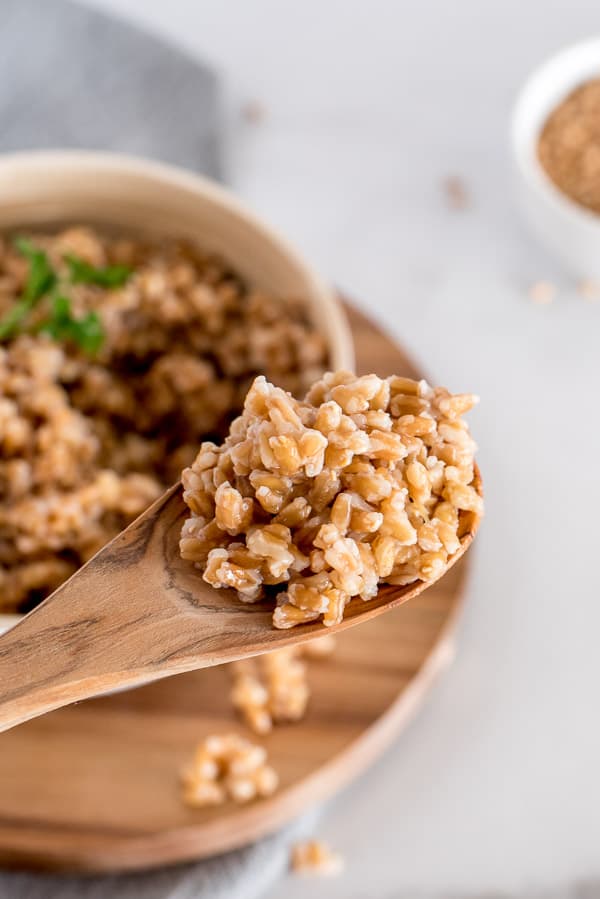 Cooked farro in a white bowl with a wooden spoon