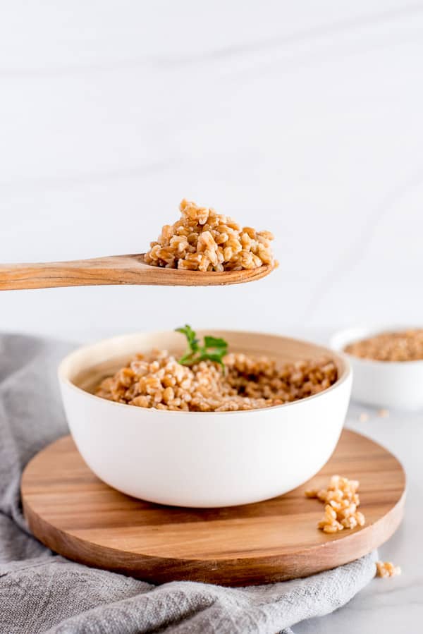 Cooked farro in a white bowl with a wooden spoon