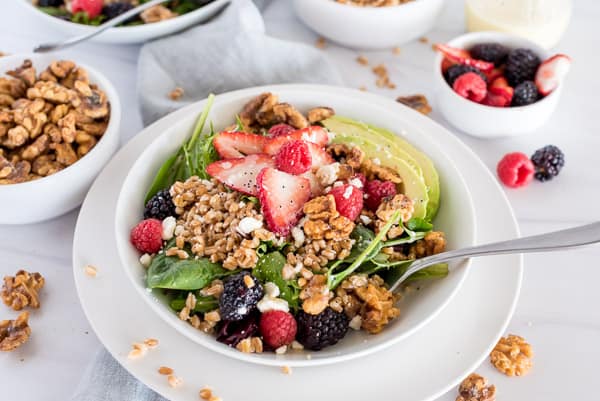 white bowl of spinach salad with raspberries, strawberries, blackberries, avocado, and walnuts