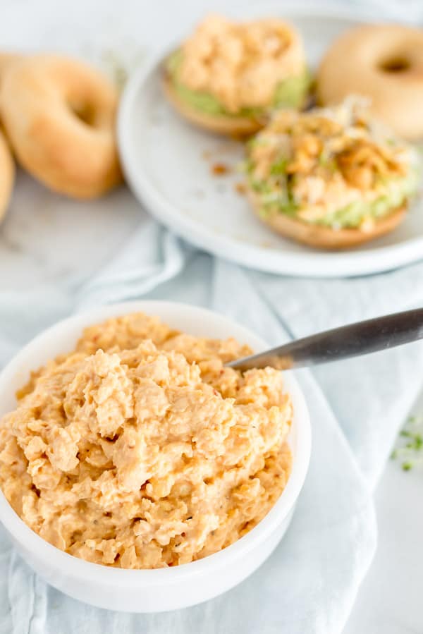 white bowl of chickpea salad with a spoon and bagels near by