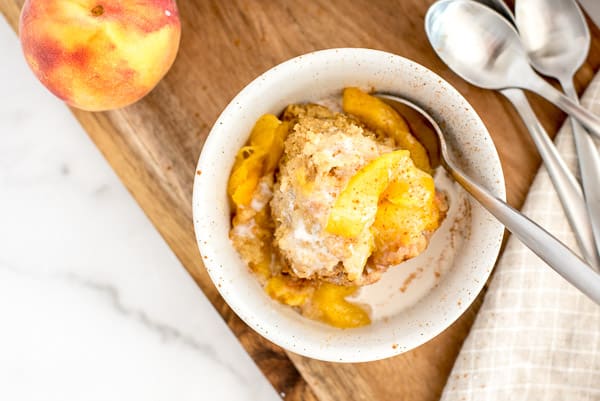 white bowl with peach cobbler, cream, and a spoon
