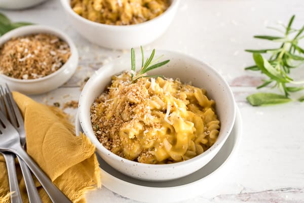 White bowl of butternut squash mac and cheese with a fork and herbs