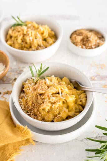White bowl of butternut squash mac and cheese with a fork and herbs