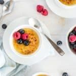creme brulee in a white ramekin with a golden crust topping and berries