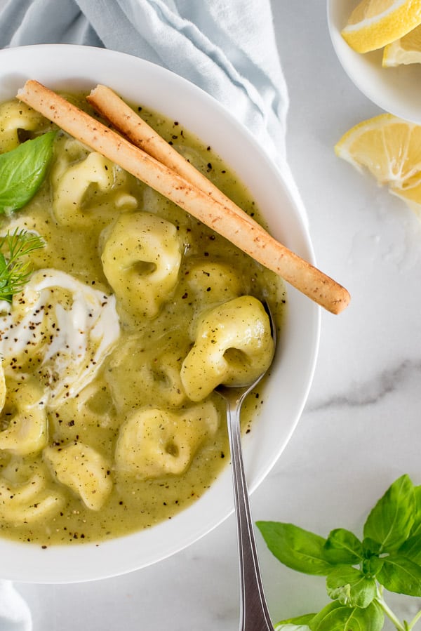 zucchini tortellini soup in a white bowl garnished with lemon and basil
